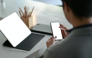 Young businessman hold a blank screen smartphone in hand and a blank screen laptop on the desk.